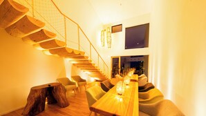 A modern interior with a wooden staircase, a dining area with a long table, and a seating arrangement. - HOTEL DO-YA BEPPU (Beppu)