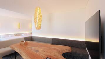 Une chambre d’hôtel moderne avec une table basse en bois, un canapé, un téléviseur fixé au mur et un luminaire suspendu original.