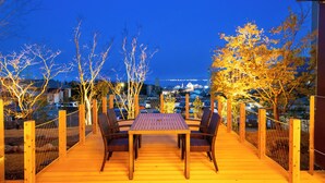 An outdoor deck with a table and chairs, surrounded by a wooden fence and trees. - HOTEL DO-YA BEPPU (Beppu)