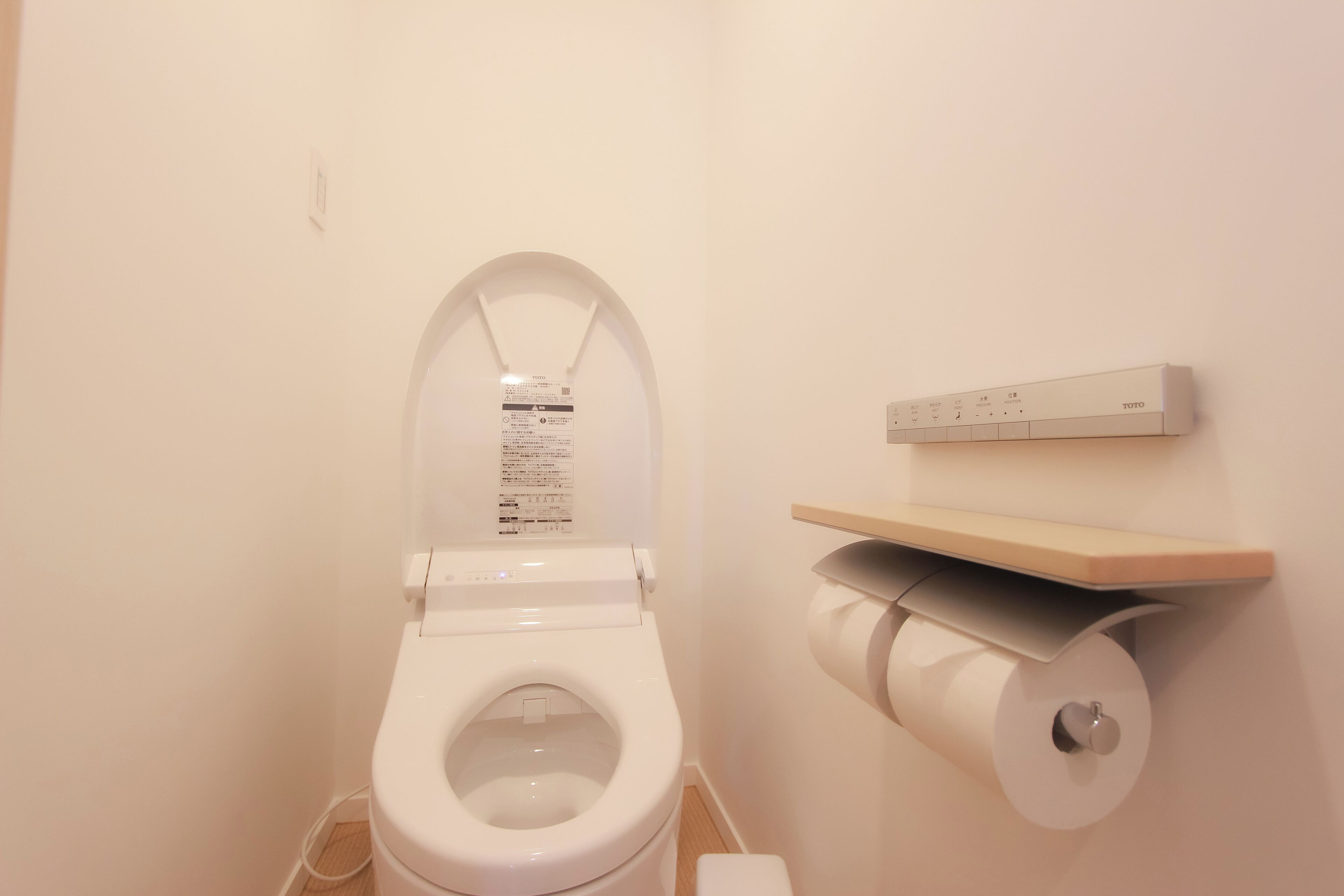 A modern bathroom with a white toilet, a toilet paper holder, and a small shelf.