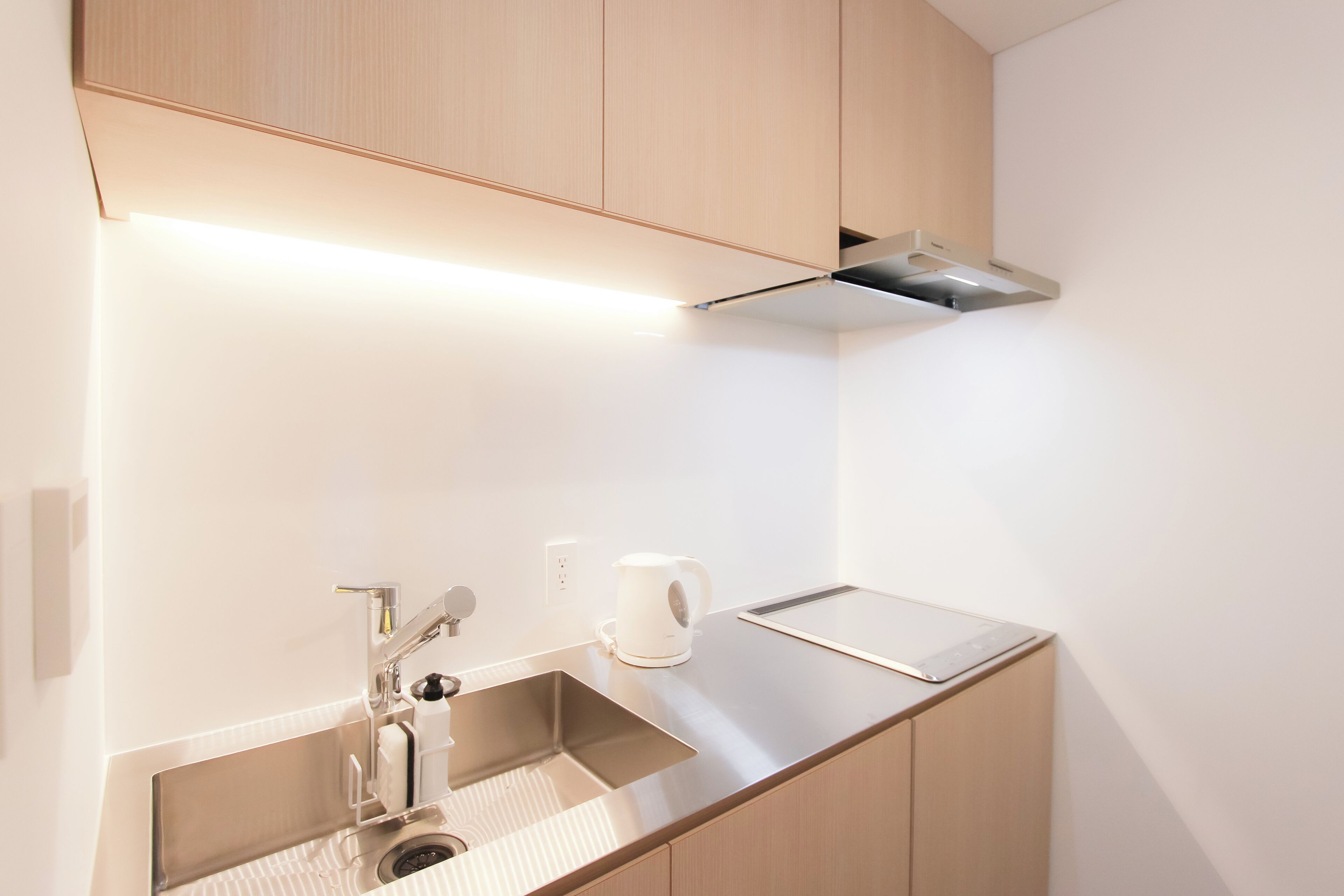 A modern kitchen with a stainless steel sink, a kettle, and a toaster on the countertop.