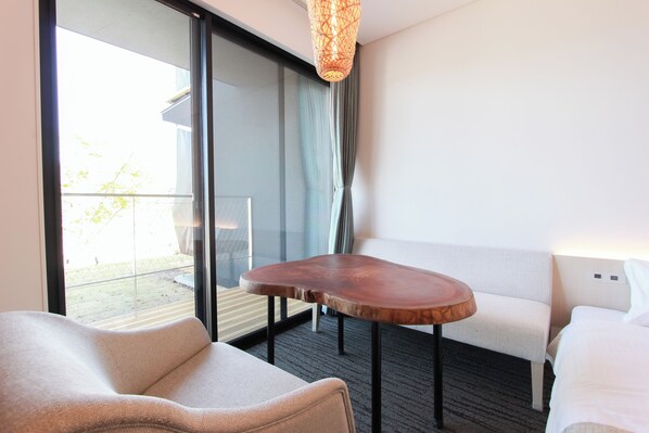 A modern hotel room with a sofa, a wooden table, and a view of the outdoors through a glass door. - HOTEL DO-YA BEPPU (Beppu)