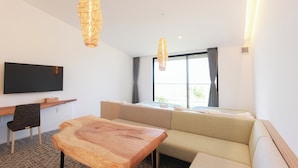 A modern living room with a wooden coffee table, a sofa, a TV mounted on the wall, and two pendant lights. - HOTEL DO-YA BEPPU (Beppu)