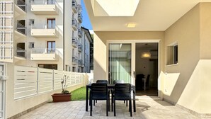 Un balcón con una mesa y sillas, una planta en maceta y vistas a un edificio con balcones.