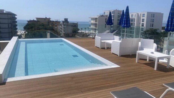 Un área de piscina en la azotea con vistas despejadas al océano, sillas de descanso blancas y sombrillas azules.