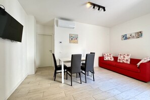 Une pièce comprenant une table à manger, quatre chaises, un canapé rouge et un téléviseur à écran plat fixé au mur.