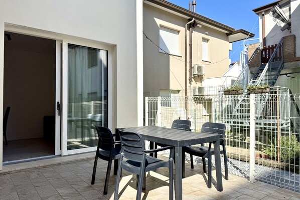 Une terrasse avec une table et des chaises, une porte-fenêtre coulissante et un espace clos avec un escalier.