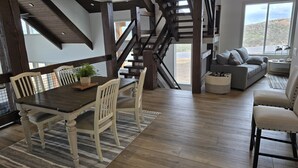 Ein geräumiger Wohnbereich mit einer Holztreppe, einem Esstisch mit Stühlen und einem grauen Sofa.