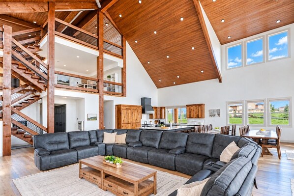 A spacious living area with a large sectional sofa, wooden flooring, and a high ceiling with exposed beams. - Timberhaven - Bear Lake Retreat - Sleeps 50+ (Fish Haven)