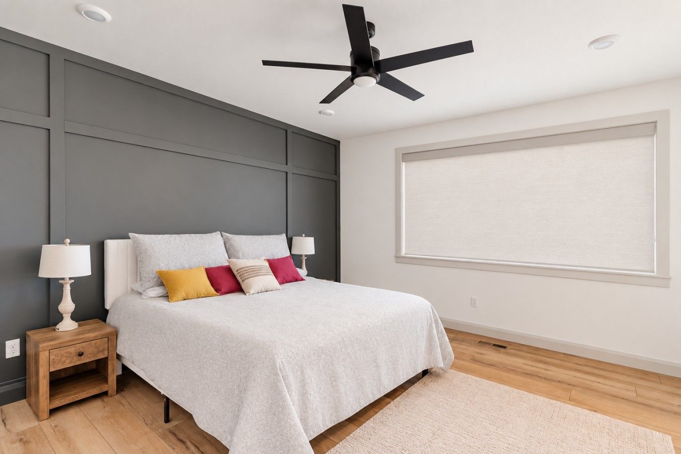 Une chambre à coucher avec un lit, des tables de chevet, un ventilateur de plafond et une grande fenêtre.