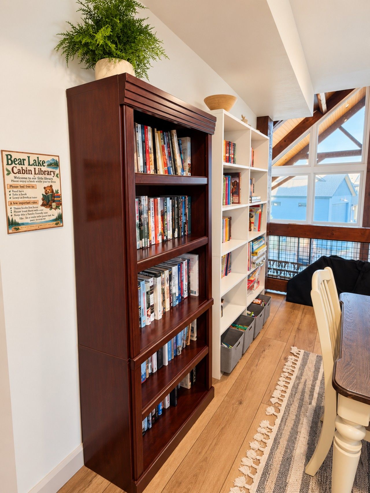 Une bibliothèque aménagée dans un chalet, avec des étagères, un coin lecture et une fenêtre donnant sur un paysage agréable.