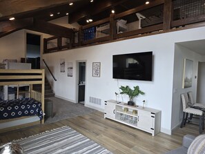 Una sala de estar moderna con una escalera de madera, un televisor montado en la pared, una consola blanca y un sofá.