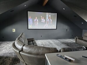 Un moderno cine en casa con una pantalla grande, asientos de cuero y un control remoto sobre una mesa.