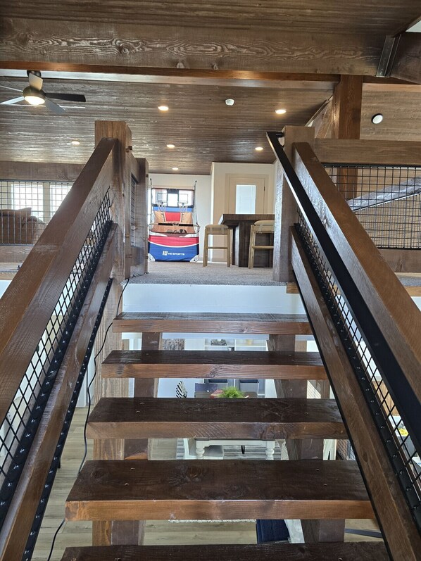 Una escalera de madera con barandales de metal que conduce a una zona de estar con vista a una cancha de baloncesto.