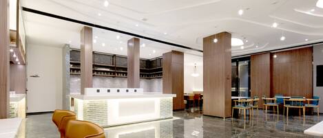 A modern hotel lobby with a reception desk, seating area, and a bar.