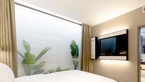 Ett hotellrum med en stor säng, en platt-TV som är monterad på väggen och ett stort fönster med gardiner.