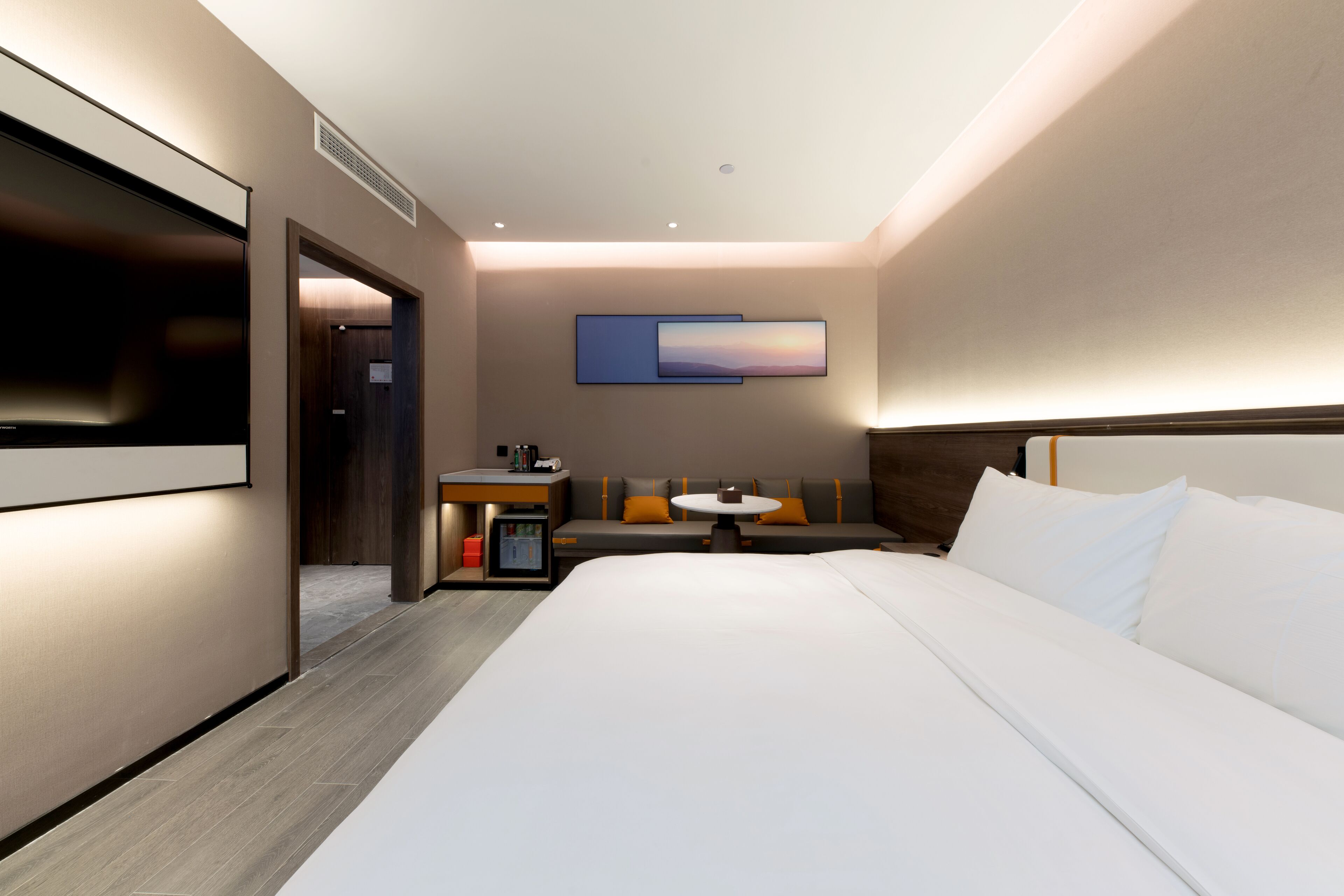 Habitación de hotel moderna con una cama grande, un escritorio con silla, una mesita y un televisor montado en la pared.