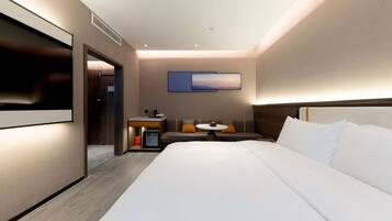 Habitación de hotel moderna con una cama grande, un escritorio con silla, una mesita y un televisor montado en la pared.