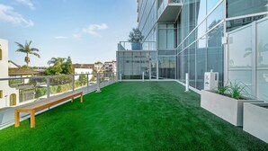 A modern building with a glass facade, a green artificial lawn, and a wooden bench.