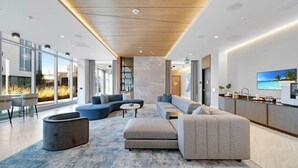 A modern hotel lobby with a large seating area, a kitchen counter, and a large window offering a view of the outdoors.