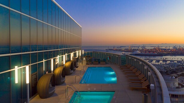 A rooftop pool with a view of a port and cityscape at sunset.