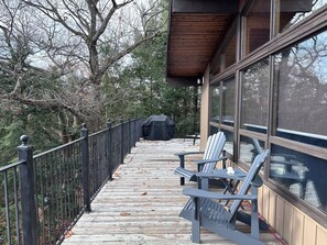 Eine überdachte Terrasse mit Adirondack-Stühlen, einem Grill und Blick auf Bäume.