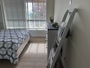 Ein Schlafzimmer mit einem Bett, einem Schminktisch, einem Spiegel und einem Fenster mit Jalousien.