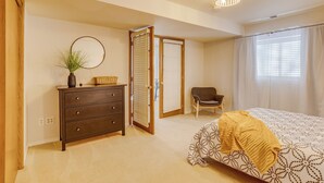 A bedroom with a bed, a dresser, a chair, and a door leading to another room. - Charming 1-bdrm walkout basement suite with AC, WiFi in lovely Colorado Springs (Colorado Springs)