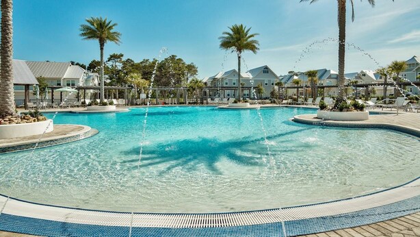 Una amplia piscina exterior rodeada de palmeras y sillas de descanso, bajo un cielo azul despejado.