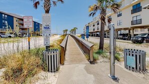Une promenade en bois mène aux bâtiments situés en bord de plage, et un panneau indique qu’elle est réservée aux véhicules d’urgence autorisés.