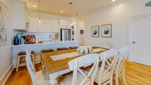 Une cuisine moderne avec des meubles blancs, une table à manger en bois et un réfrigérateur.