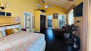 A bedroom with a large bed, a ceiling fan, and a view into the kitchen.