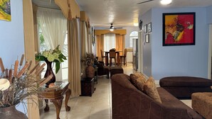 A spacious living room with a brown sofa, a dining area with wooden chairs, and a ceiling fan.