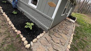 A house with a gray exterior, a welcome sign, and a stone pathway leading to the entrance.