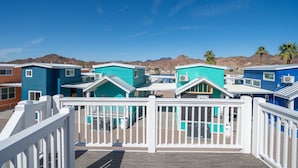 A row of colorful beach houses with white railings, a clear blue sky, and mountains in the background. - Blue Bliss, Private Hot Tub & Fenced Yard at Roadrunner Resort (Parker)