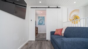 A modern living room with a blue sofa, a painting of a shell on the wall, and a staircase leading to another room. - Blue Bliss, Private Hot Tub & Fenced Yard at Roadrunner Resort (Parker)