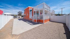 A modern house with a red exterior and white balcony railings, surrounded by a white fence.