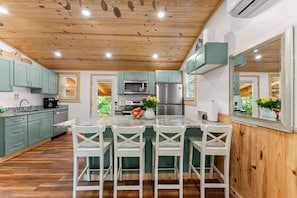 A modern kitchen with a wooden ceiling, granite countertops, and a central island with bar stools.