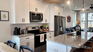 A modern kitchen with white cabinets, stainless steel appliances, granite countertops, and bar seating. - Charming & Spacious Townhome on North College Street in Auburn (Auburn)
