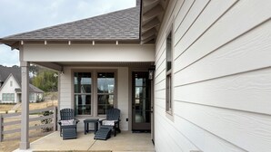 A covered porch with two Adirondack chairs and a small table, a sliding glass door, and a view of a residential area. - Charming & Spacious Townhome on North College Street in Auburn (Auburn)