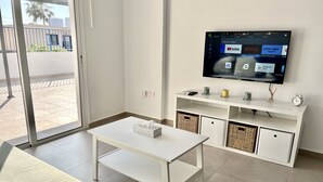Una sala de estar moderna con un televisor de pantalla plana montado en la pared, una mesa blanca y un sofá.