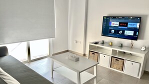 Una sala de estar moderna con un sofá blanco, una mesa de centro y un televisor en la pared que muestra aplicaciones populares.