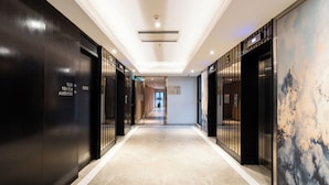 A modern hotel corridor with a long hallway, black elevator doors, and a large abstract mural on the right wall. - Luxury D1 Mension Condotel (Ho Chi Minh City)