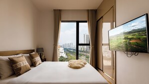 A hotel room with a large bed, a TV on the wall, and a view of a cityscape through the window. - Luxury D1 Mension Condotel (Ho Chi Minh City)