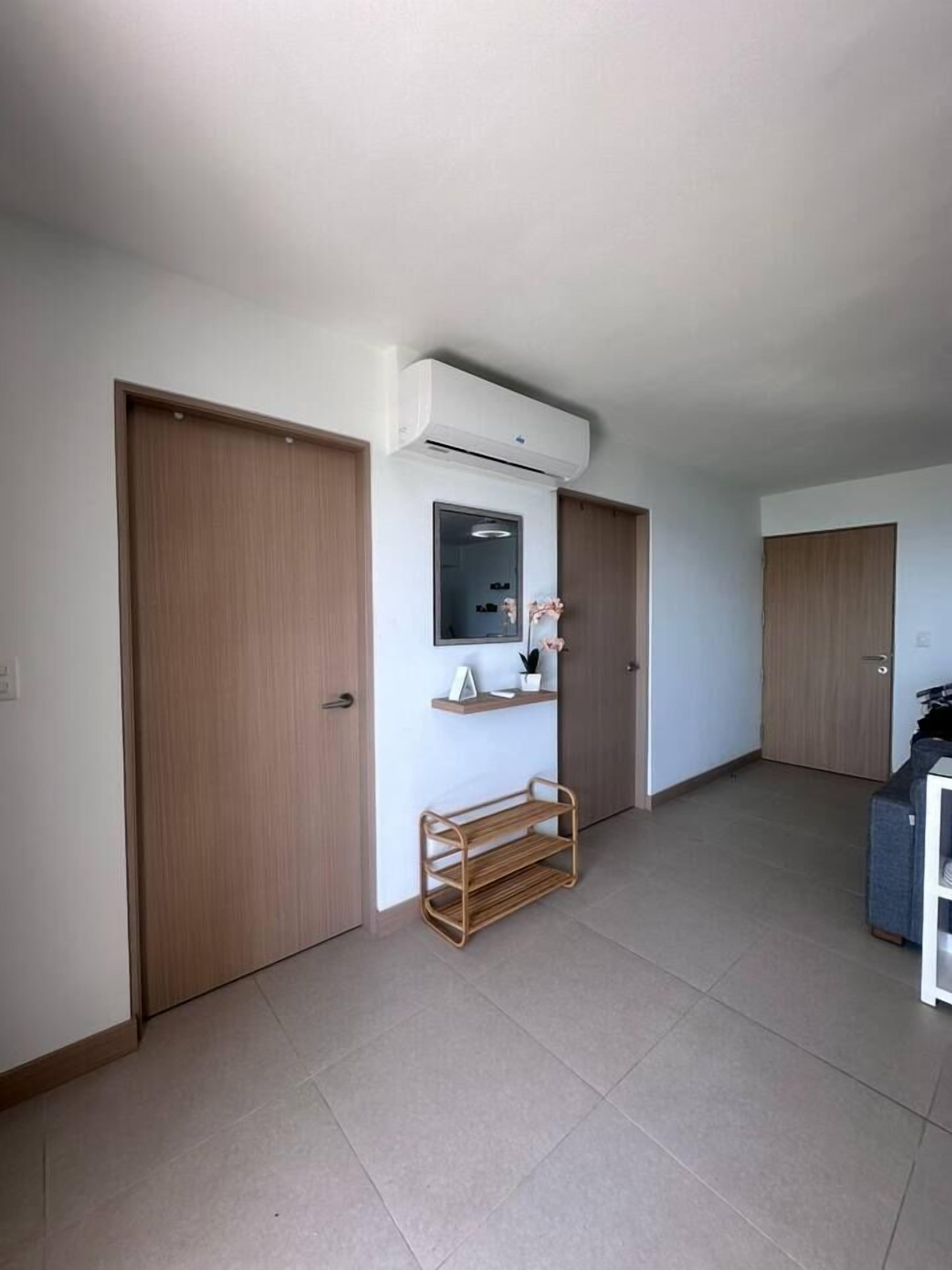 Ein Flur mit Holztüren, einer Wand-Klimaanlage, einem kleinen Regal mit Dekoration und einem Holzständer.