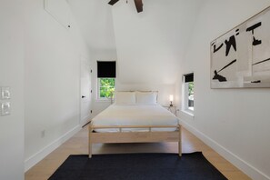 Een slaapkamer met een bed, een raam, een kunstwerk aan de muur en een deur naar een andere kamer.