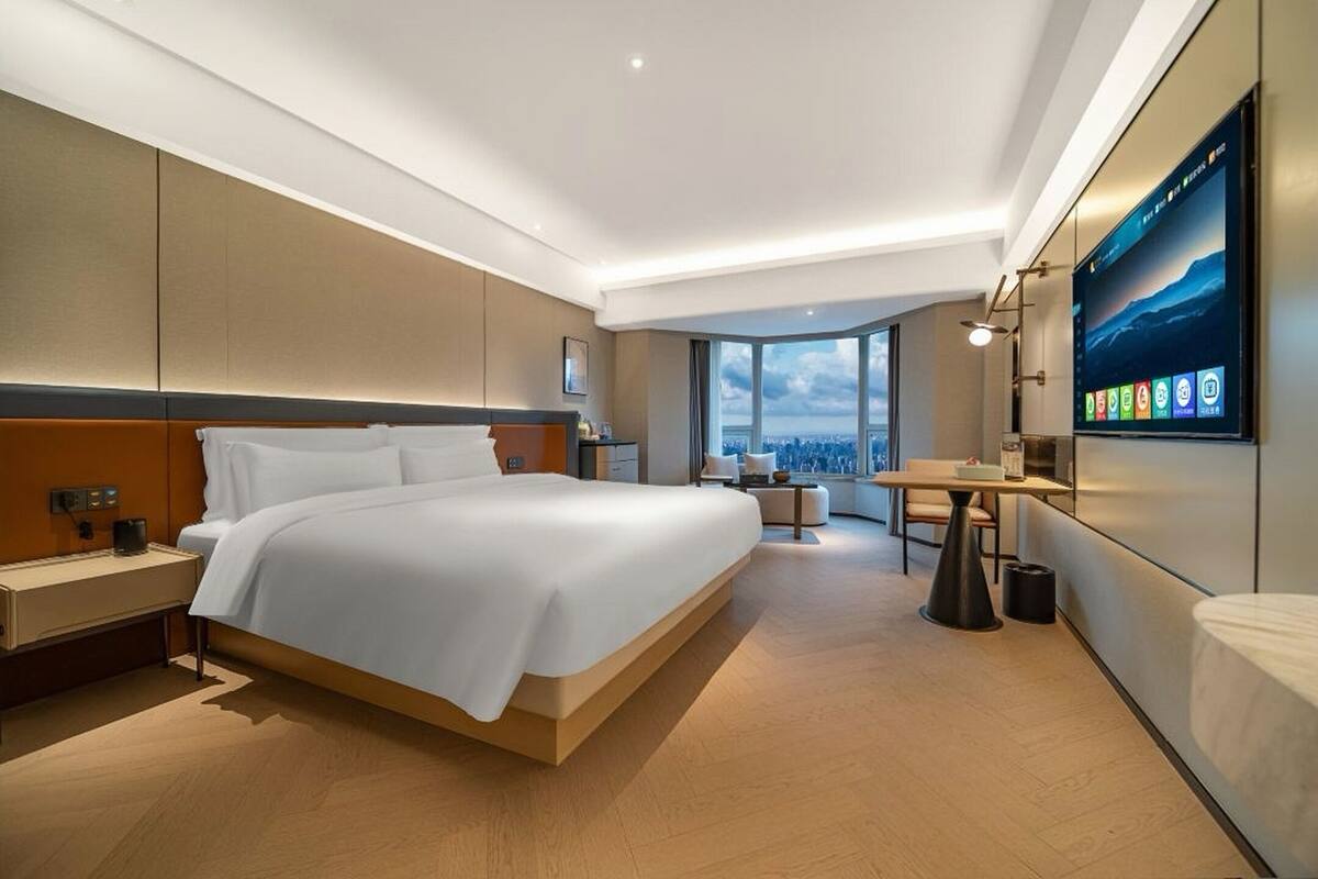 Habitación de hotel moderna con una cama grande, un escritorio, un televisor y vistas a la ciudad.