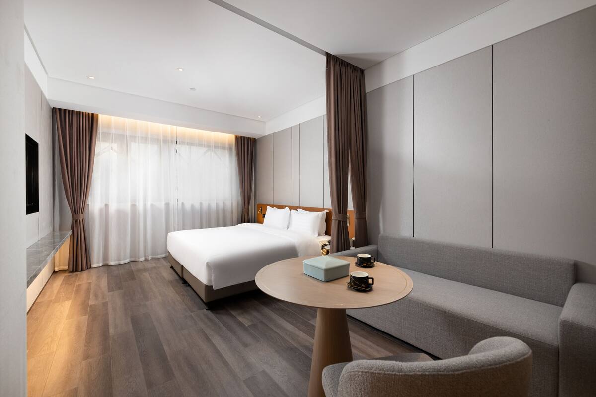 Una habitación de hotel moderna con una cama grande, un sofá, una mesa redonda con una taza de café y cortinas.