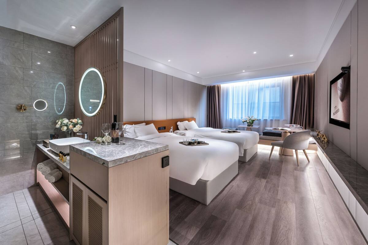 Una habitación de hotel moderna con baño, dos camas, un escritorio y una silla.
