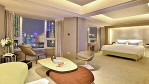 A modern hotel room with a city view, a large bed, a desk with a chair, and a small table with a vase and fruit. - Elegant International Hotel Shanghai - Bund Sichuan Road North Metro Station Branch (Shanghai)
